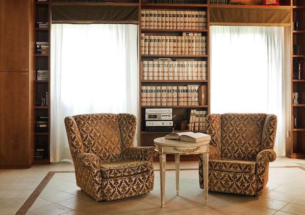 Une bibliothèque avec deux fauteuils à motifs, une petite table ronde et des étagères remplies de livres et de cassettes.