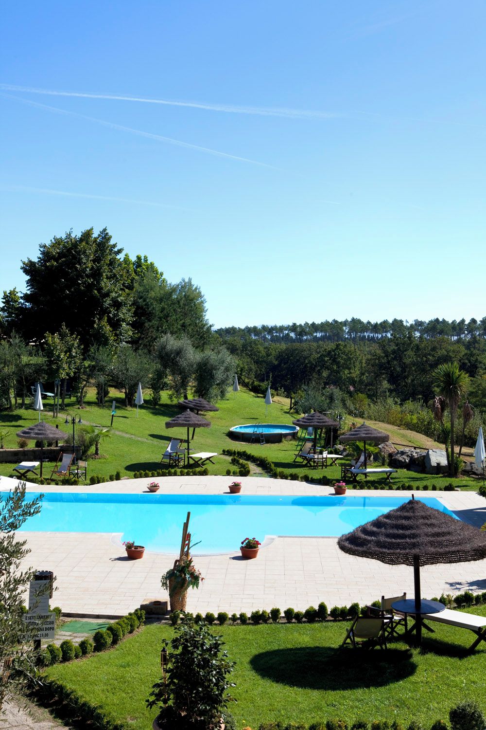Área de piscina com espreguiçadeiras e guarda-sóis, cercada por vegetação e árvores.