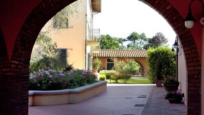 An arched pathway leading to a building with a tiled roof, surrounded by potted plants and flowers. - Assia Spa (Fucecchio)