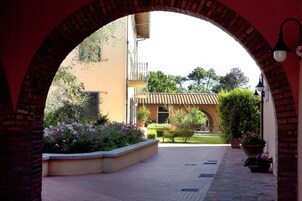 Un sendero arqueado que conduce a un edificio con tejado de baldosas, rodeado de macetas con plantas y flores.