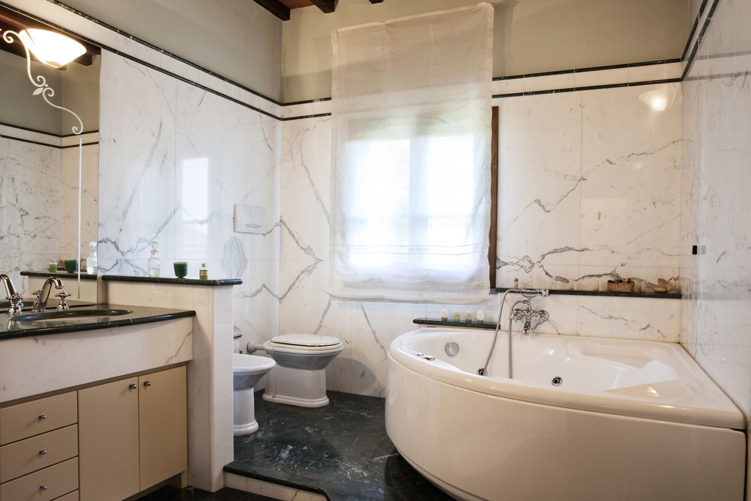 A bathroom with a marble wall, a bathtub, a toilet, and a sink with a mirror.