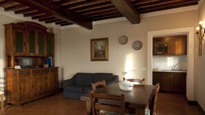 A dining area with a wooden table and chairs, a sofa, and a kitchen with wooden cabinets and a tiled backsplash. - Agriturismo La Colombaia (Cerreto Guidi)