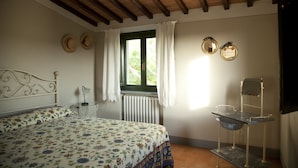 A bedroom with a bed, a small bedside table, a window with curtains, a radiator, and a chair with a tray. - Agriturismo La Colombaia (Cerreto Guidi)