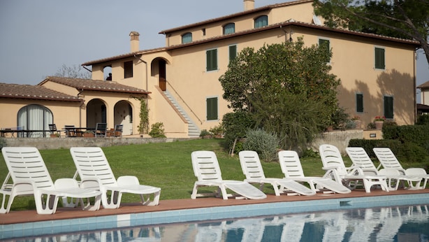 A poolside area with white lounge chairs and a large building with multiple windows and a staircase. - Agriturismo La Colombaia (Cerreto Guidi)