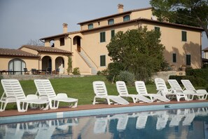 A poolside area with white lounge chairs and a large building with multiple windows and a staircase. - Agriturismo La Colombaia (Cerreto Guidi)