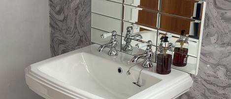 A bathroom with a white pedestal sink, a mirror with a wooden frame, and a marble-patterned wall.