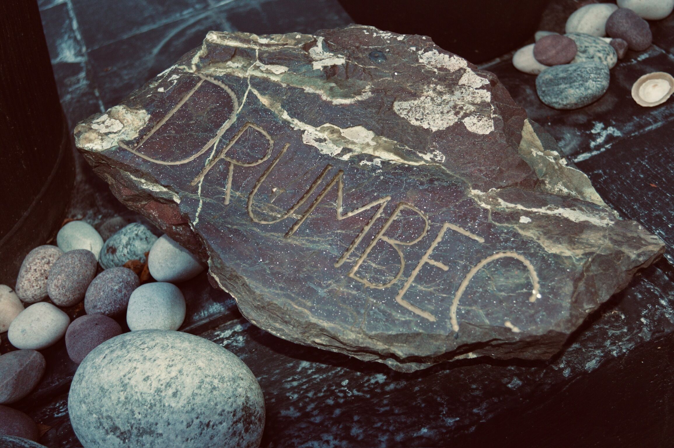 Un rocher portant l’inscription « DRUMBEQ », entouré de petits galets.