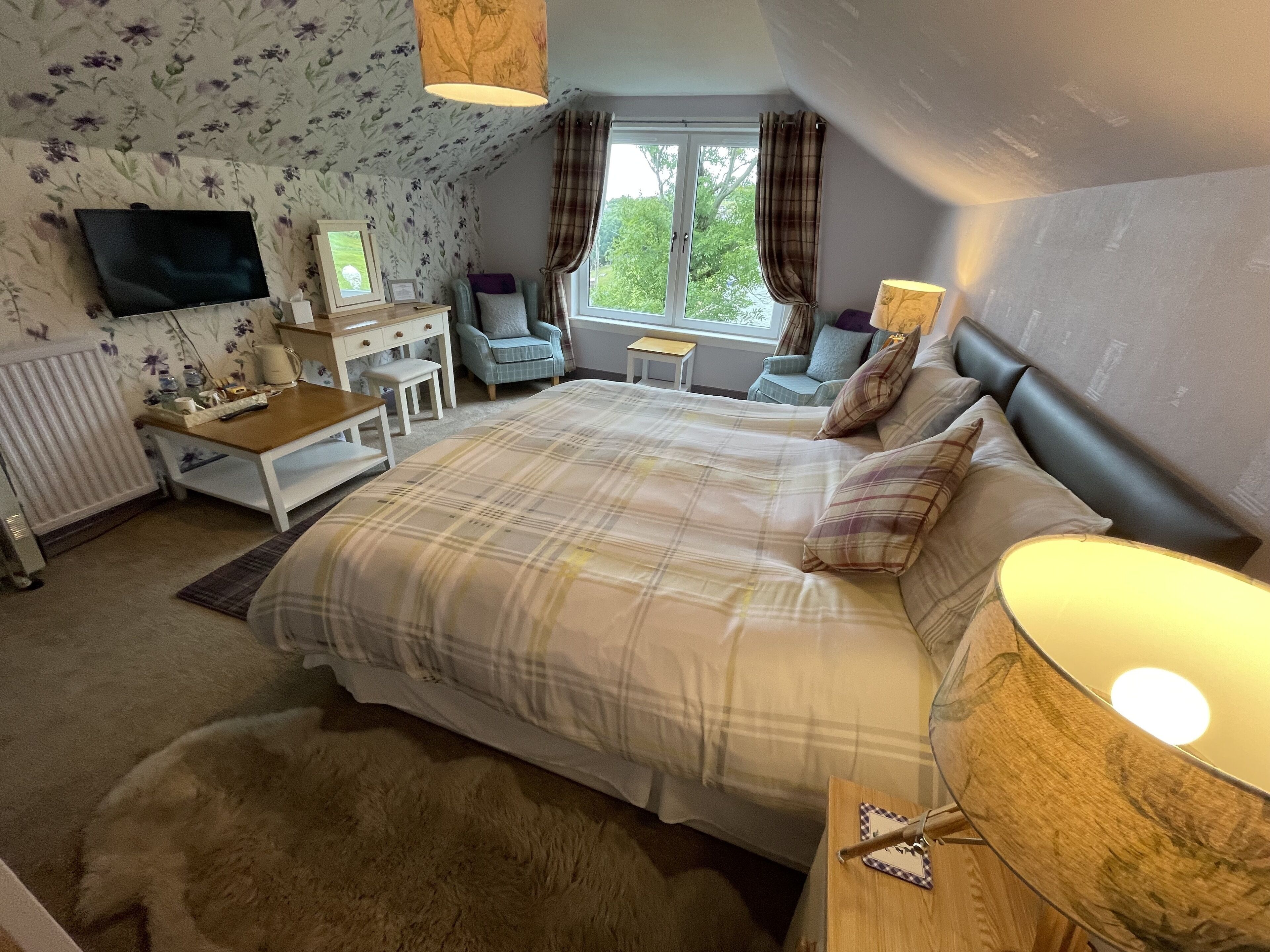 Ein Schlafzimmer mit einem großen Bett, einem Schreibtisch, einem Stuhl, einem Fenster mit Vorhängen und einer Heizung.