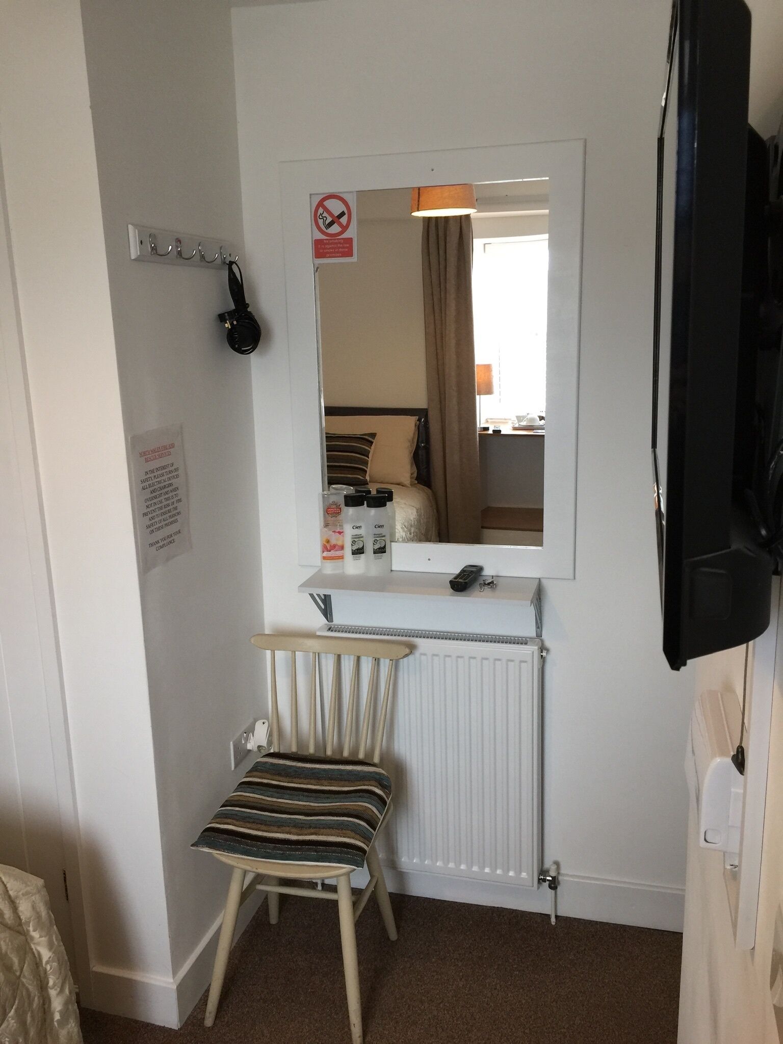 A compact hotel room with a bed, a small desk with a mirror, a chair, and a radiator.
