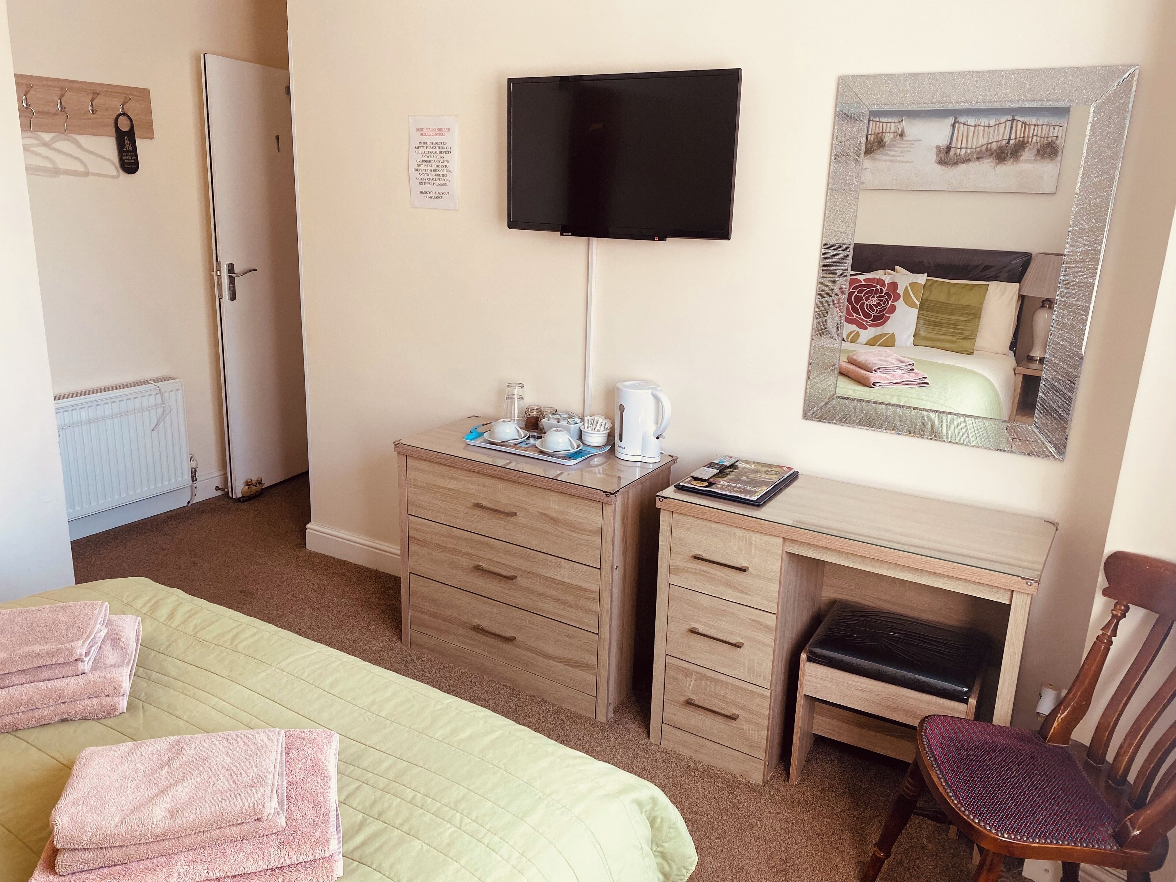 Une chambre d’hôtel comprenant un lit, un bureau avec des tiroirs, une chaise, un téléviseur, un radiateur et un tableau encadré au mur.