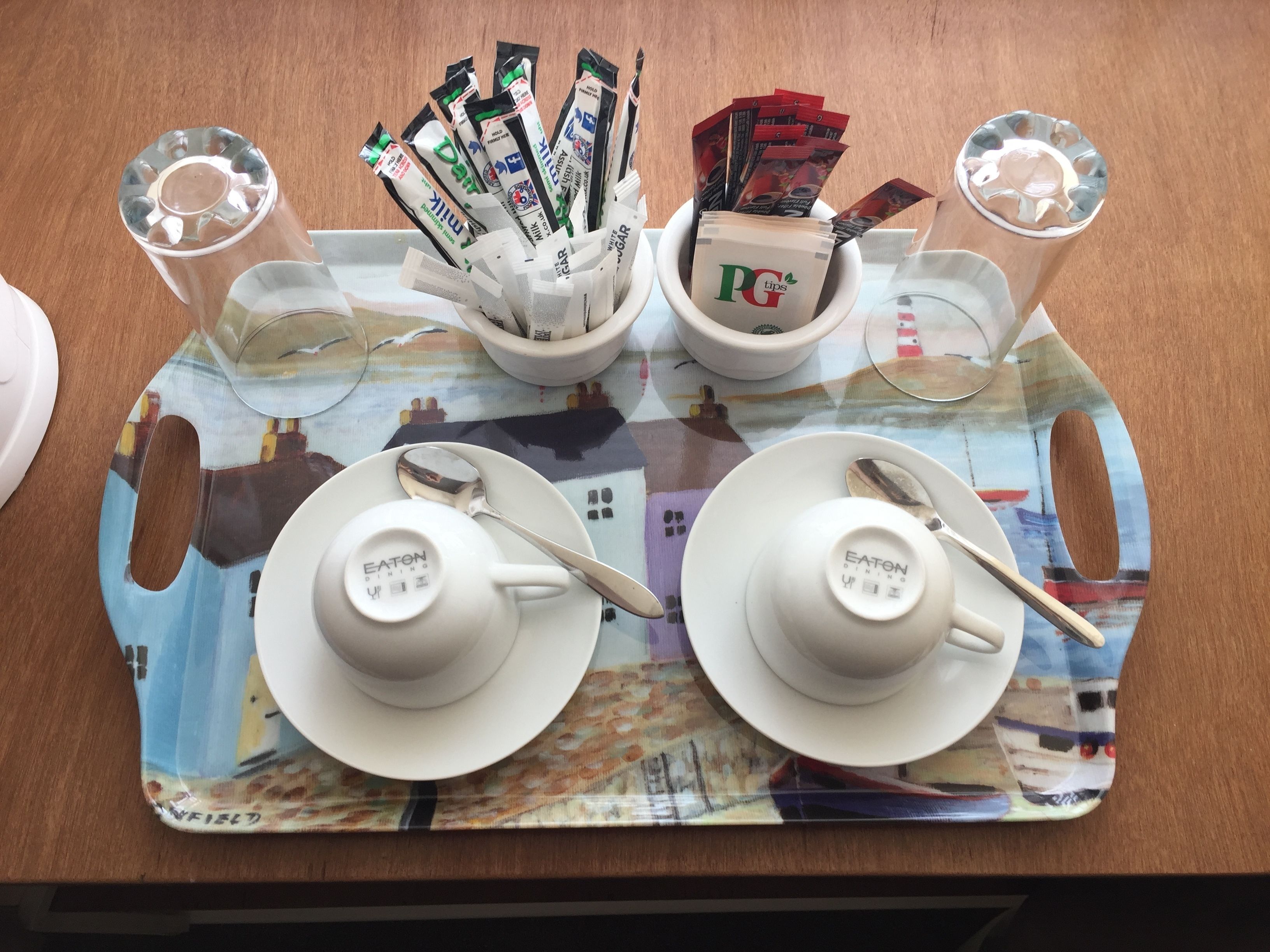 Una bandeja con dos tazas blancas con la etiqueta 'EATON DINING', una cuchara y sobres de té PG tips.