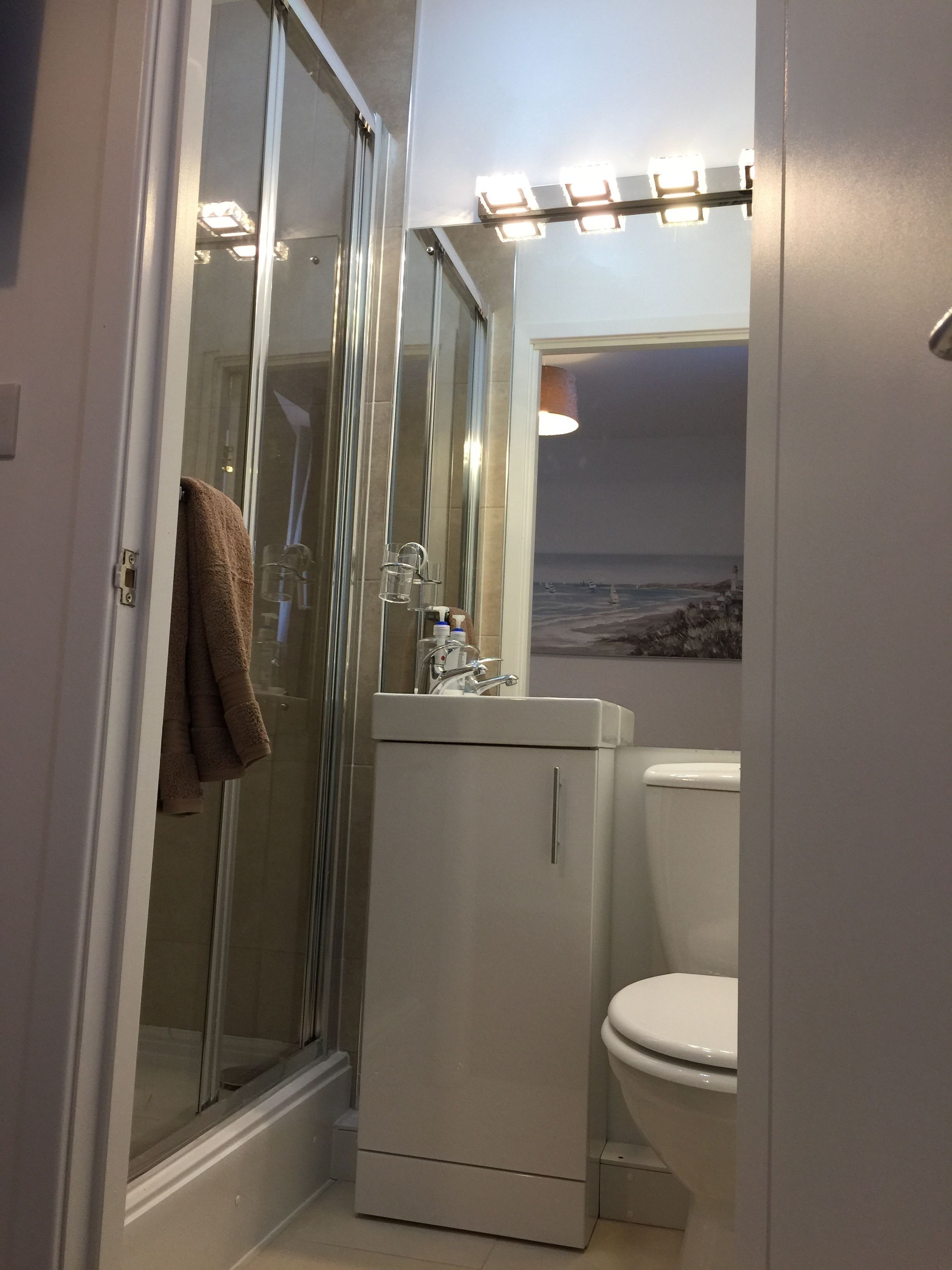 Kylpyhuone, jossa on lasinen suihkuovi, peilillä varustettu pesuallas ja wc.