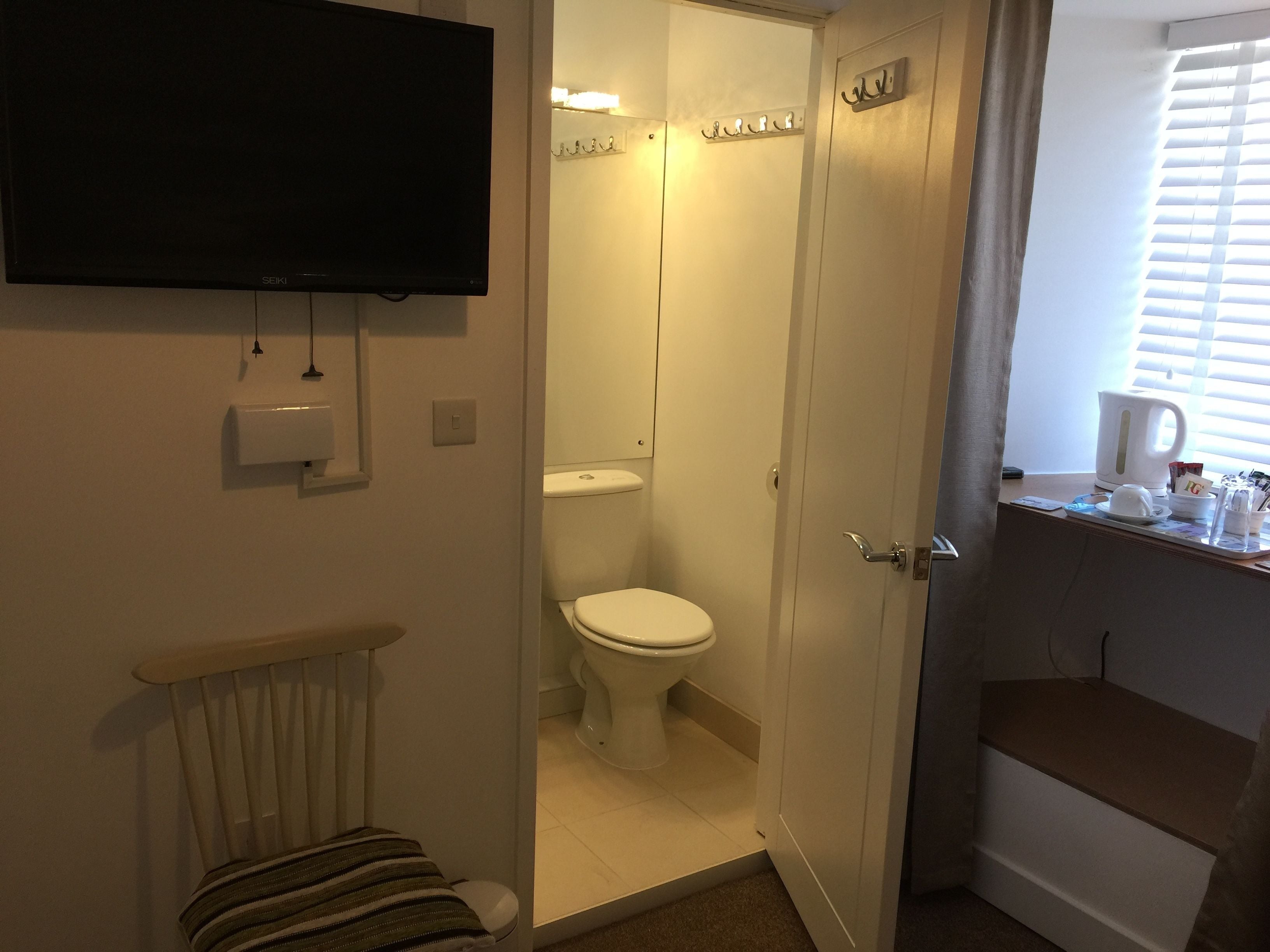 Ein Badezimmer mit Toilette, Dusche, Waschbecken, Spiegel und einem an der Wand montierten Fernseher.