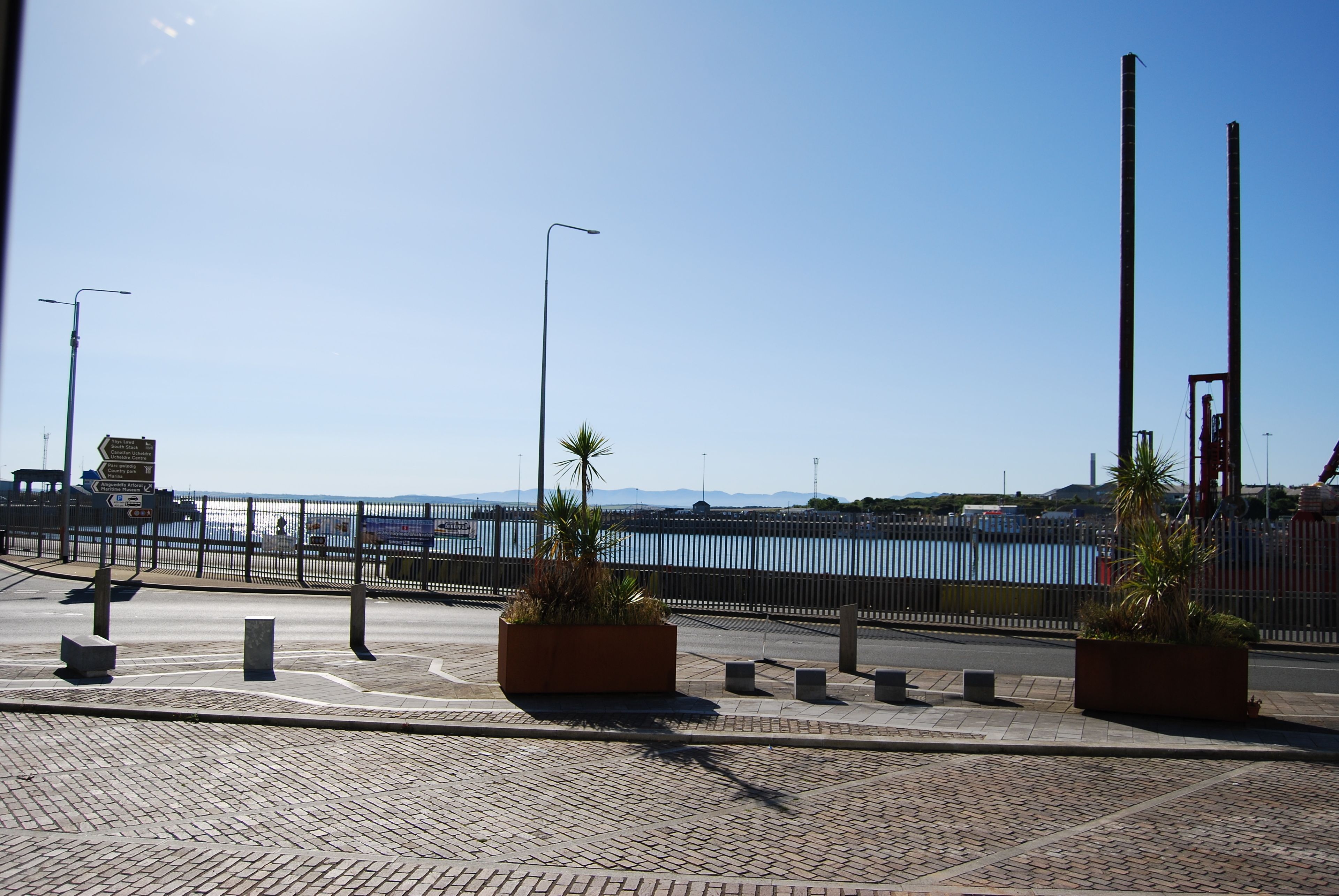 Une promenade en bord de mer, dallée, agrémentée d’une clôture en métal, de lampadaires et de jardinières.