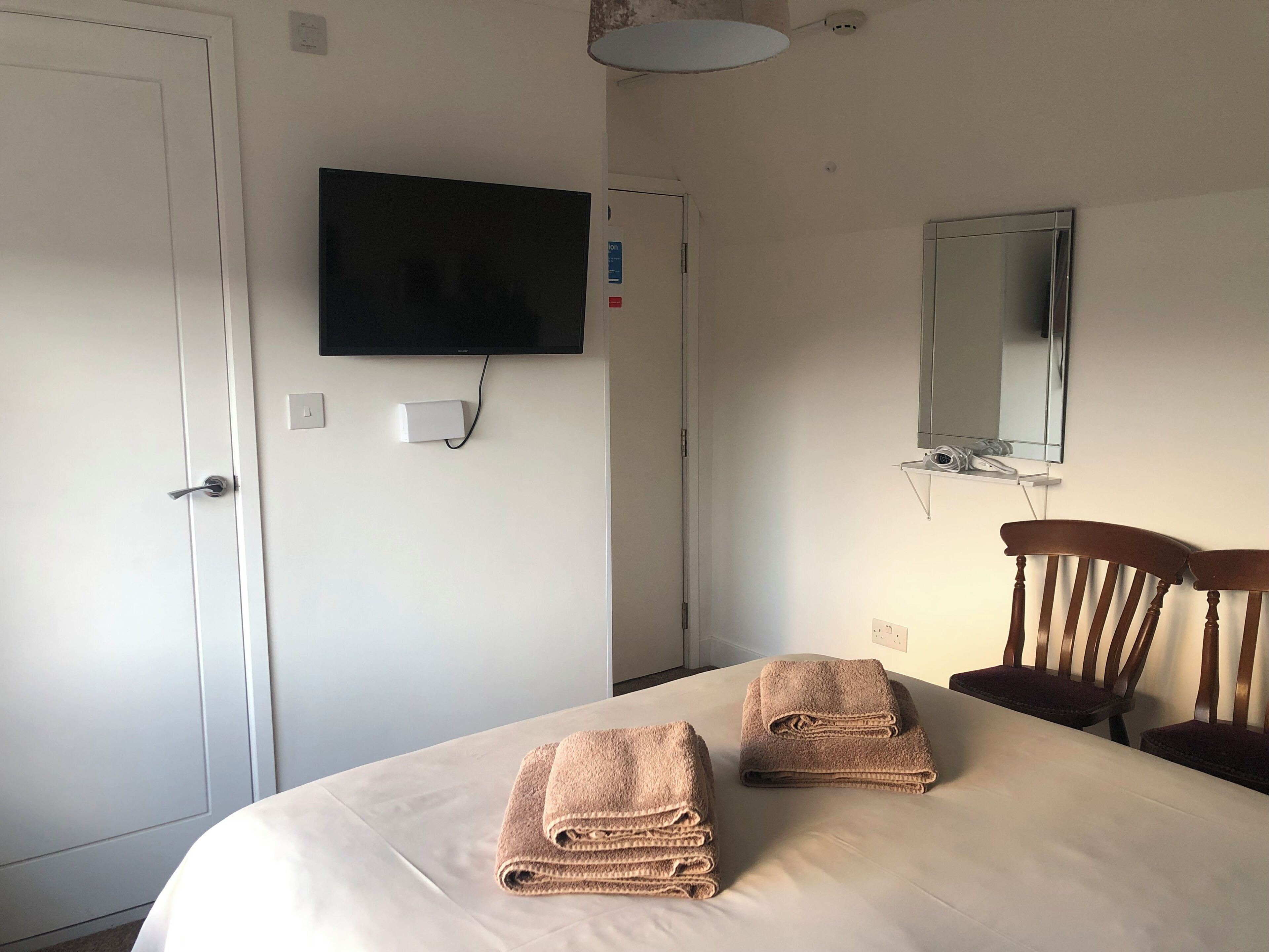 A hotel room with a bed, a TV mounted on the wall, a mirror, and two chairs.