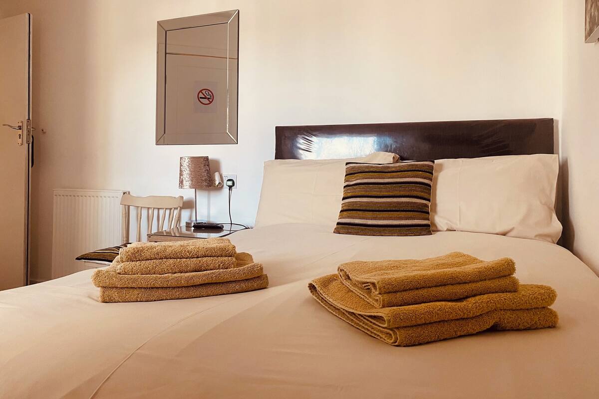 Habitación de hotel con una cama bien hecha, una silla, una lámpara y un cartel de prohibido fumar en la pared.
