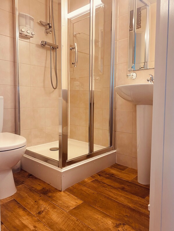 A modern bathroom with a glass-enclosed shower, a white toilet, and a sink with a mirror above it. - The Haven Guest House (Holyhead)
