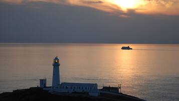 A lighthouse at sunset with calm sea and a ship in the distance.