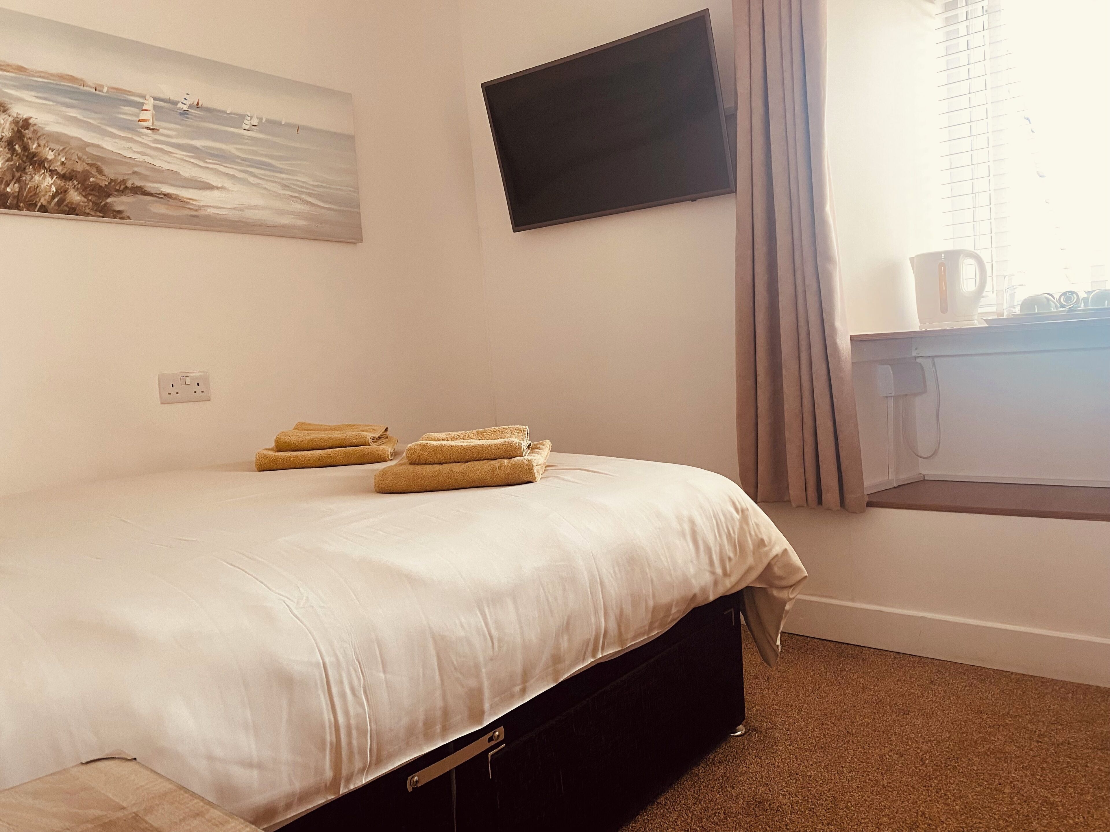 A neatly made bed with a white comforter and several folded towels. A flat-screen TV is mounted on the wall above the bed.