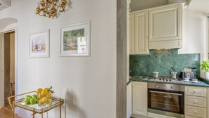 A kitchen with white cabinets, a green marble countertop, and a stove. There is a small table with fruit and a picture frame on the wall. - Benedetto Duomo (Florence)