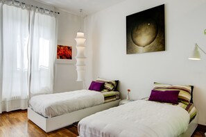 A bedroom with two beds, a wall-mounted lamp, a painting, and a window with curtains. - Porta Garibaldi B&B (Milan)