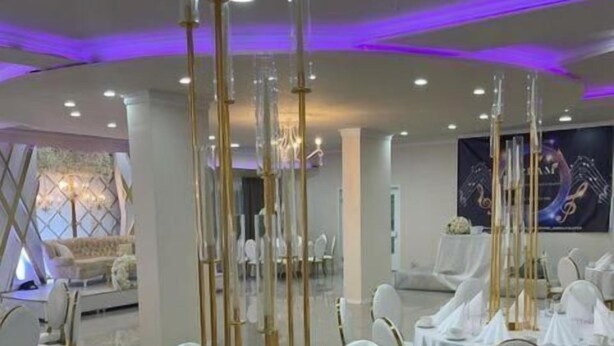 Une salle de banquet avec des tables rondes recouvertes de nappes blanches, des chaises dorées et de hauts luminaires élancés en forme de bougies.