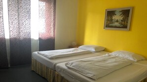 Une chambre avec deux lits, un tableau au mur et une fenêtre ornée de rideaux à motifs.