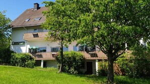 Un immeuble à plusieurs étages doté de balcons, d’un jardin et d’un arbre au premier plan.