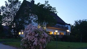 Un bâtiment à deux étages doté d’un balcon, entouré d’arbres et d’une pelouse bien entretenue.