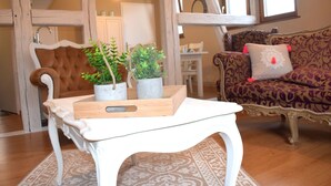 Un salon avec une table blanche, deux plantes en pot, un tapis à motifs, un canapé marron avec un coussin et un fauteuil à motifs.