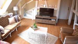 Un salon chaleureux avec un ensemble de canapés, un téléviseur posé sur un meuble en bois, un tapis à motifs et un escalier agrémenté d’une lampe décorative.
