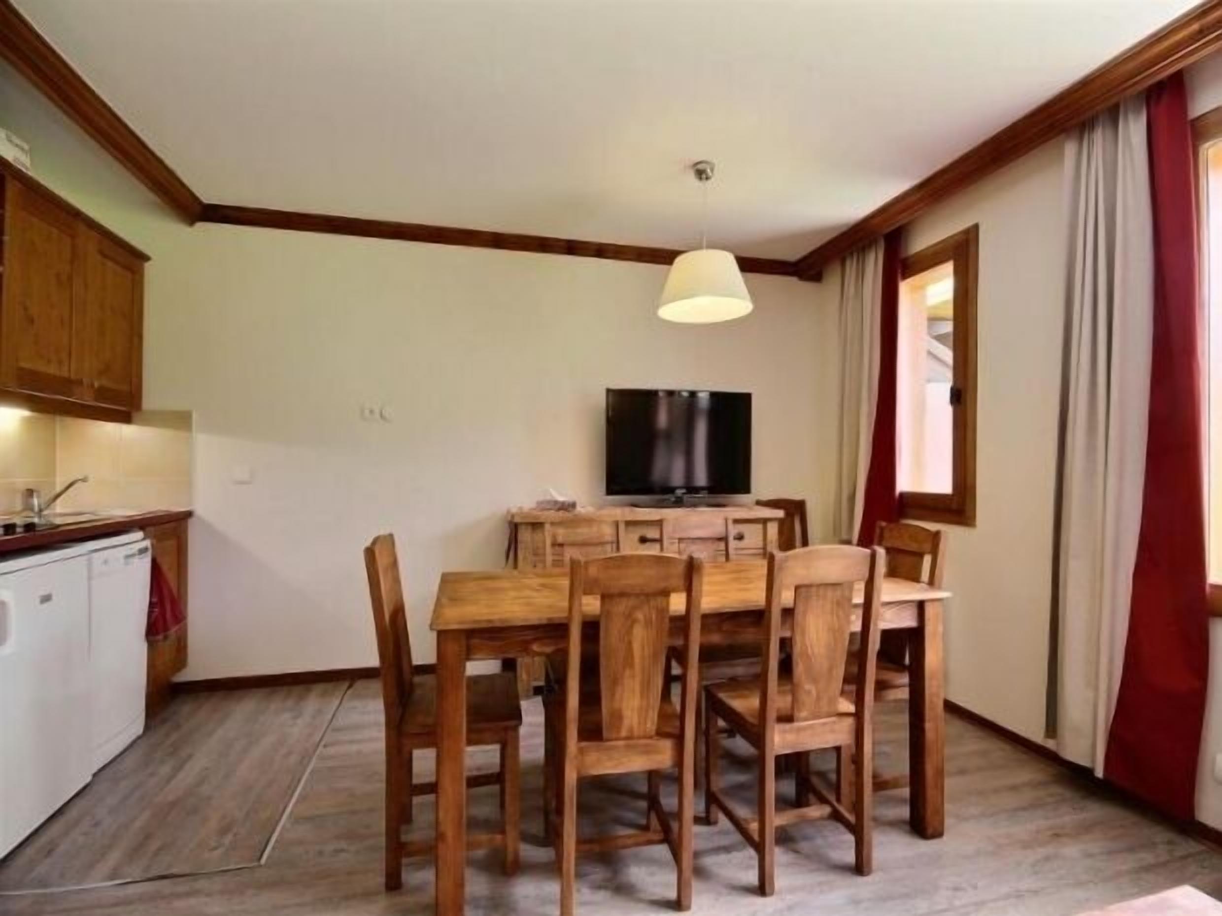 A compact kitchen with a dining area, a television, and wooden furniture.