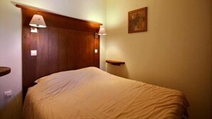 A hotel room with a wooden headboard, a bed with a beige blanket, a nightstand with a lamp, and a painting on the wall. - 3-room apartment, 2 bathrooms, direct access to slopes (Plagne Soleil)