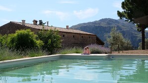 Ein Schwimmbecken mit einem Steinhaus im Hintergrund und Bergen in der Ferne.