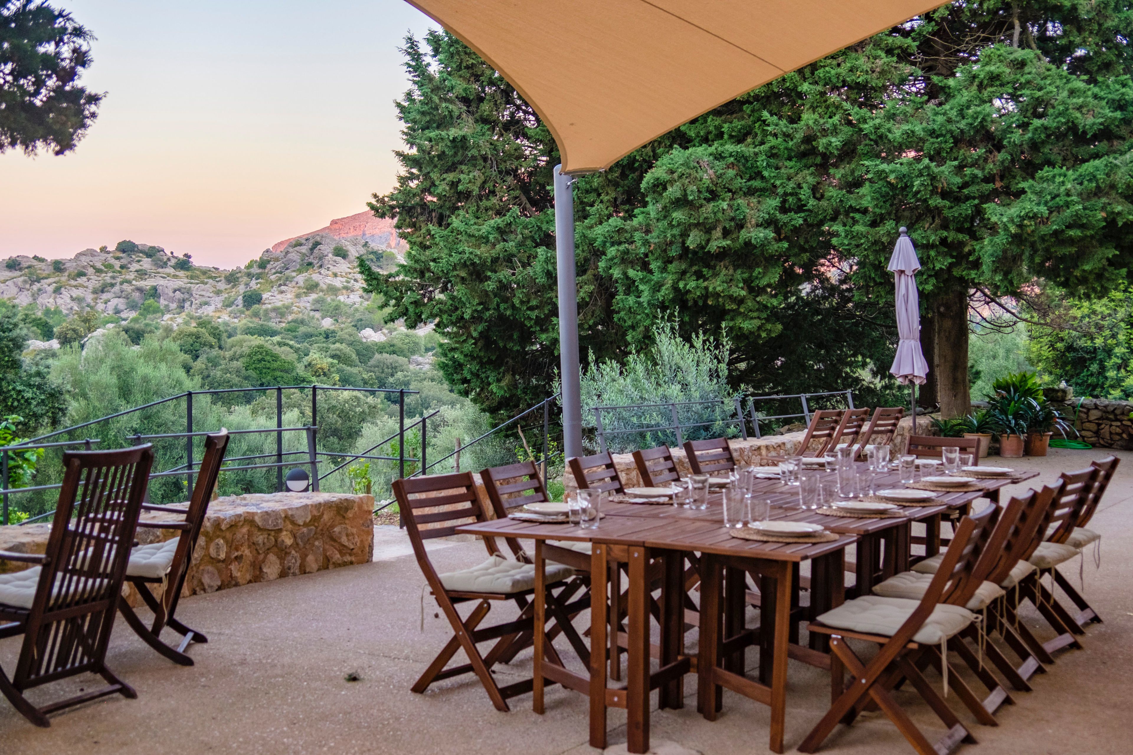 Un área de comedor al aire libre con una mesa larga preparada para seis personas, rodeada de sillas de madera con asientos acolchados.