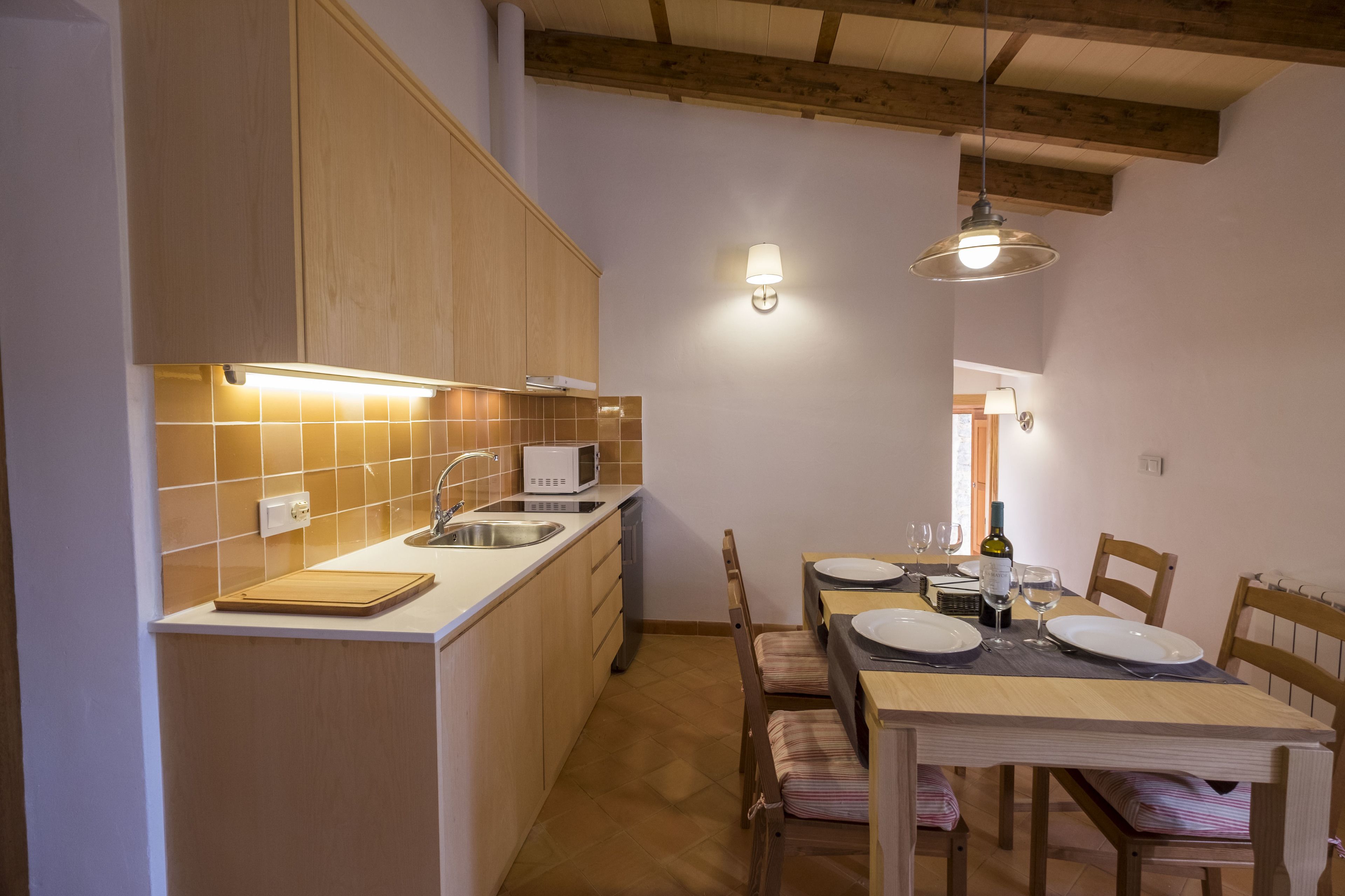 A compact kitchen with wooden cabinets, a white countertop, and a dining area with a table set for two.
