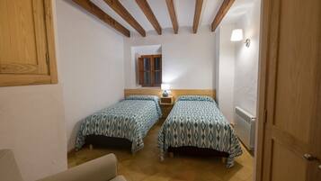 Une chambre avec deux lits, des poutres en bois au plafond, une fenêtre et un radiateur.