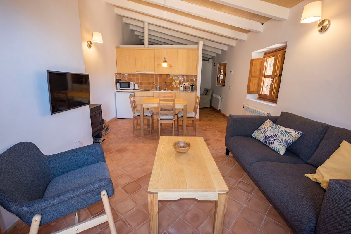 Un espacio habitable compacto con un sofá, una mesa de comedor y un televisor montado en la pared.