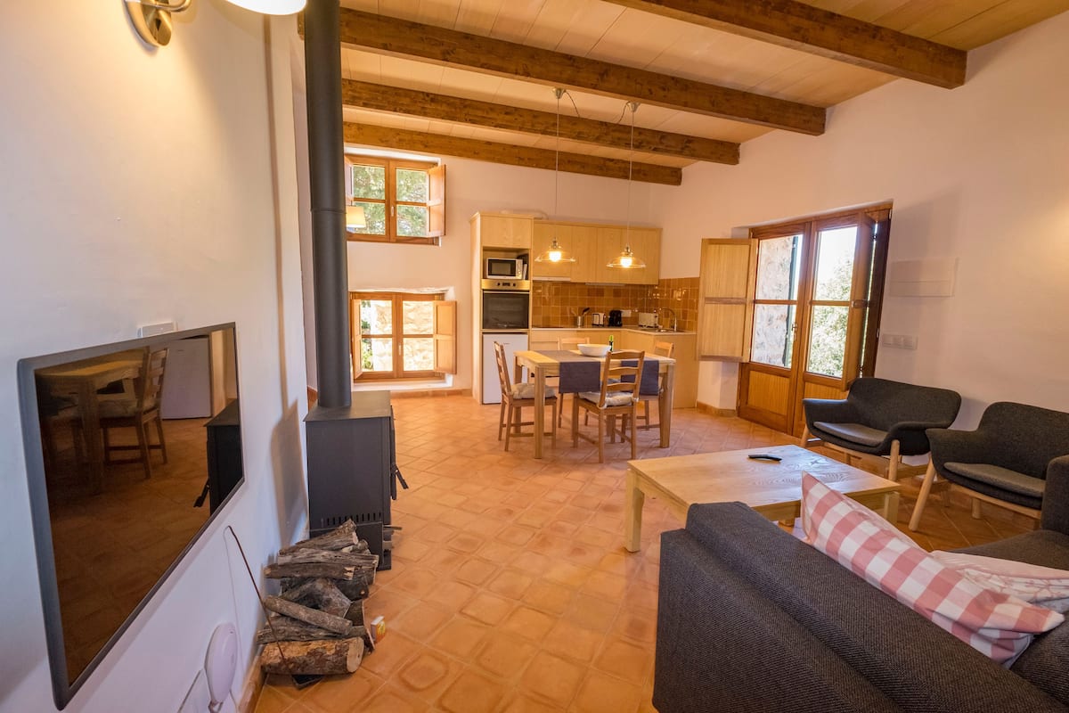 Una sala de estar acogedora con chimenea, comedor y cocina con armarios de madera y un ventanal grande.