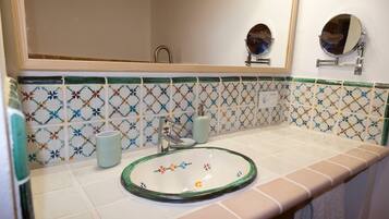 Un baño con un lavabo de vidrio redondo, un espejo y un salpicadero de azulejos con diseño floral.