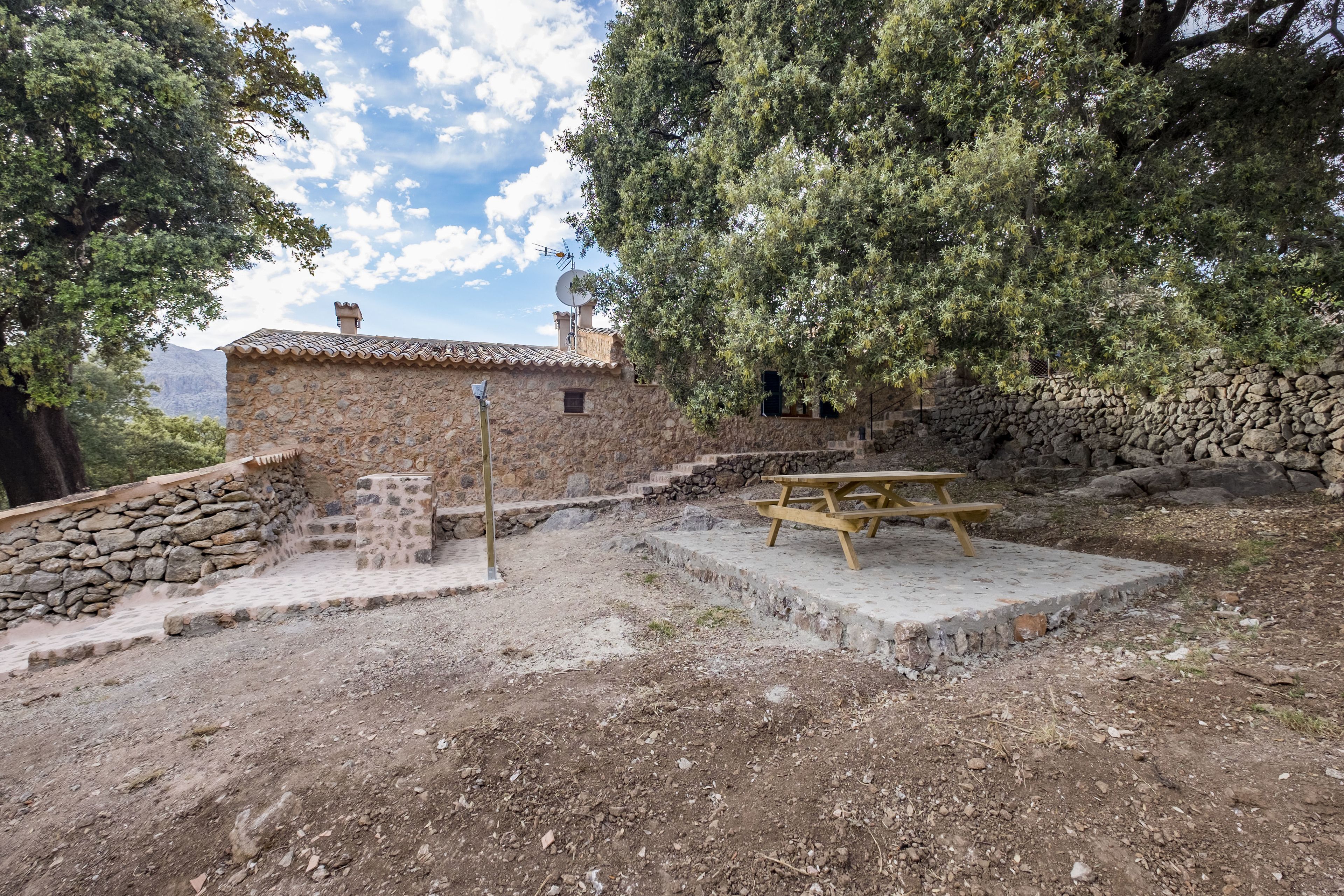 A rustic stone building with a tiled roof, a picnic table, and a stone wall.