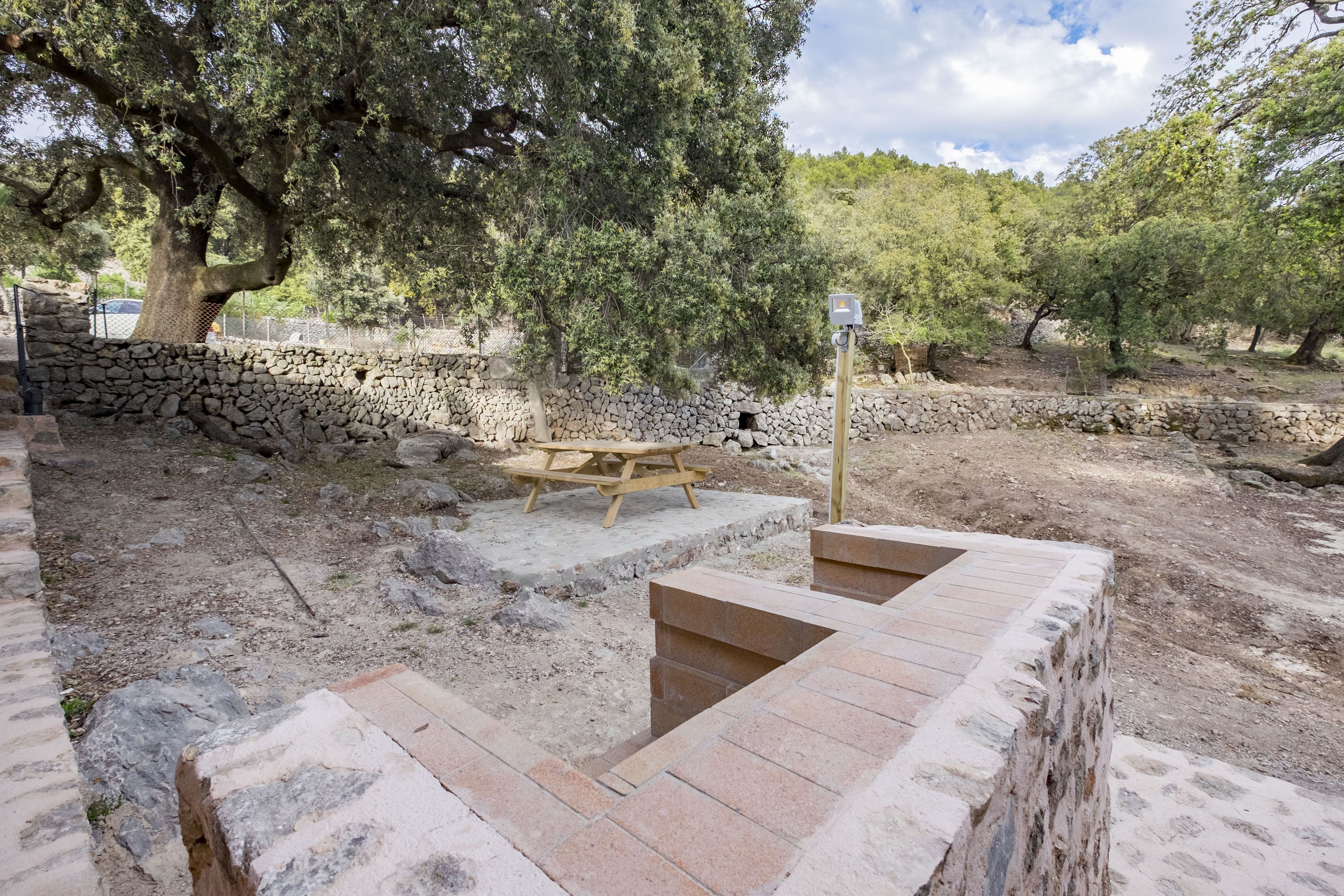 Un muro de piedra con una mesa de picnic y escalones que conducen a una plataforma de madera.