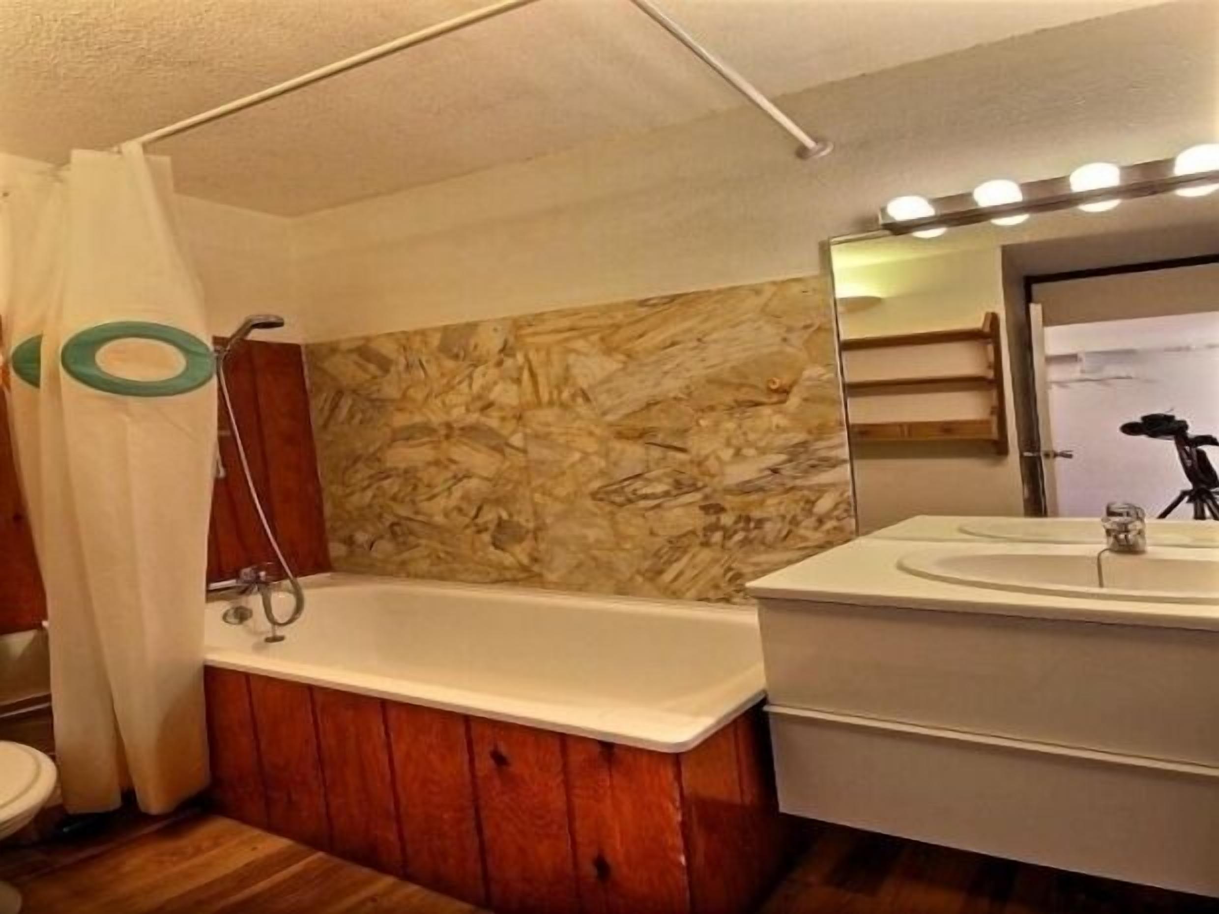 A bathroom with a wooden vanity, a bathtub, and a mirror with lights above the sink.