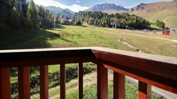 Une vue depuis un balcon donnant sur un paysage montagneux, avec une route et des bâtiments visibles au loin.