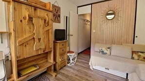Une pièce de taille modeste, avec une armoire en bois, un lit, une petite table ronde et un miroir au mur.