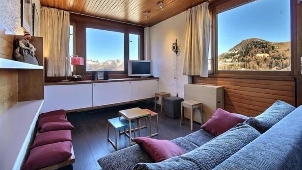 Una habitación acogedora con techo de madera, un sofá, una mesita y un televisor.