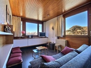 Une pièce chaleureuse avec un plafond en bois, un canapé, une petite table et un téléviseur.