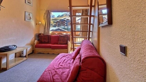 A cozy room with a wooden ceiling, a red sofa, a small table, and a window with a view of buildings. - Duplex for 5/6 at the slopes with balcony (La Plagne)