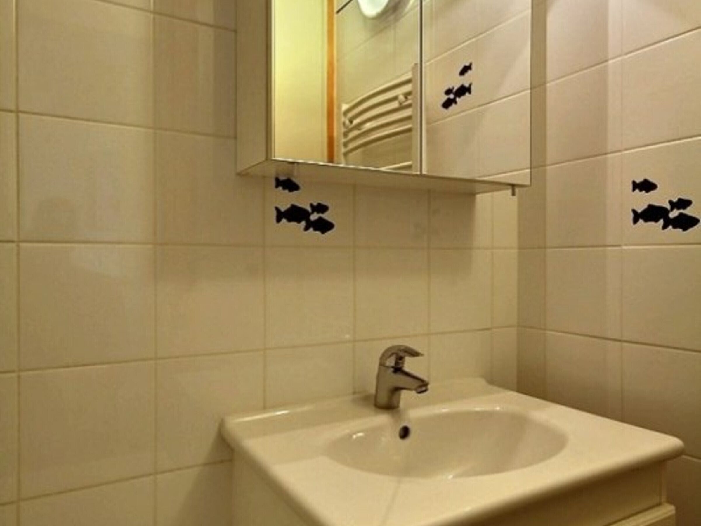 Een badkamer met een wastafel, spiegel en betegelde wanden met visstickers.
