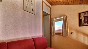 A room with a red sofa, a framed picture on the wall, and a window with curtains. - Duplex for 5/6 at the slopes with balcony (La Plagne)